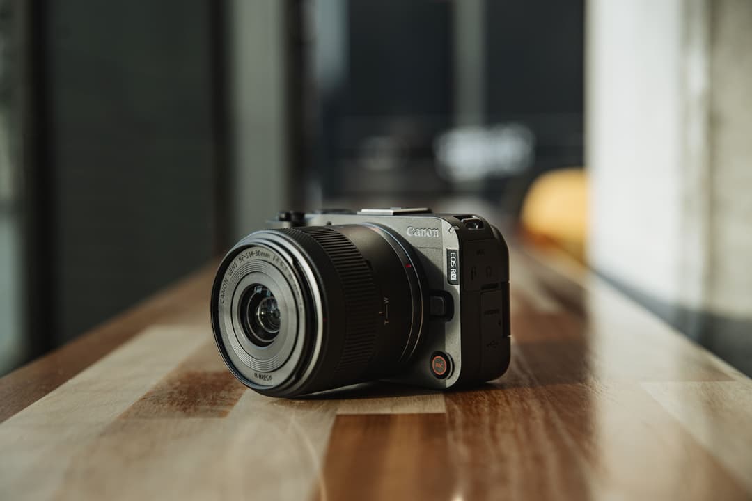 Caméra Canon compacte noire et grise posée sur une table en bois, objectif visible, arrière-plan flou
