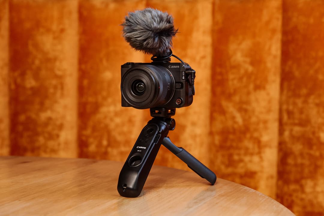 Canon EOS R50 V montée sur un stabilisateur avec microphone, sur fond orange