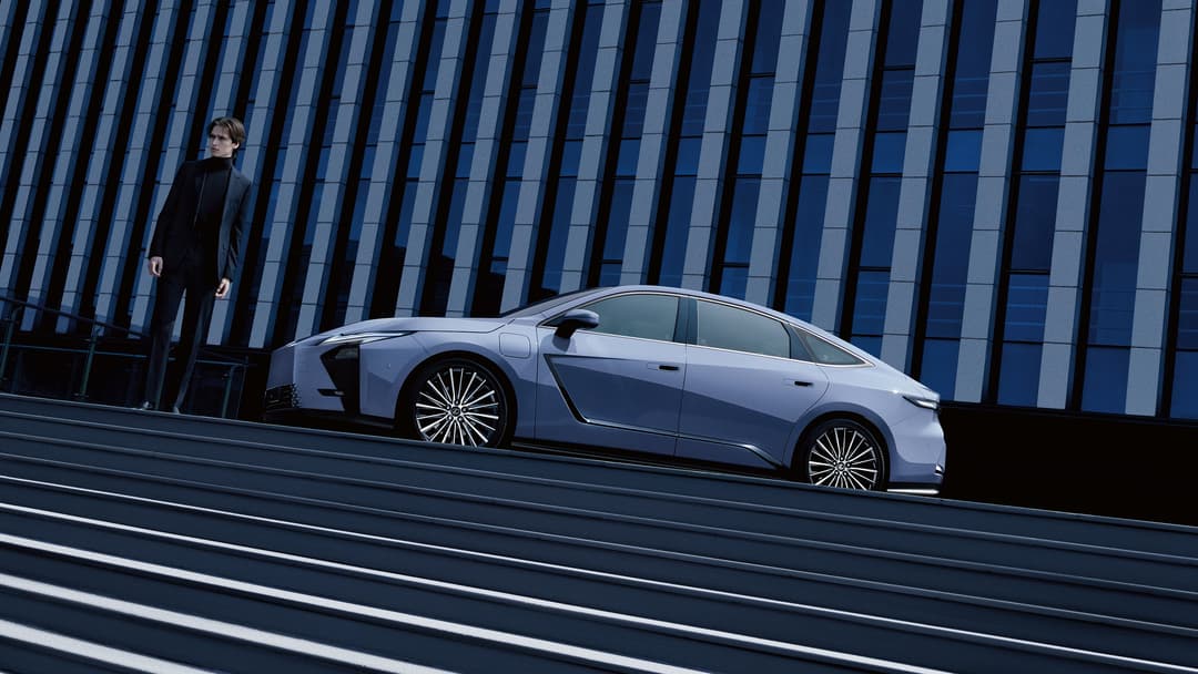 Nouvelle Lexus ES argentée garée devant une façade bleue à motifs géométriques, avec un homme en costume noir à proximité