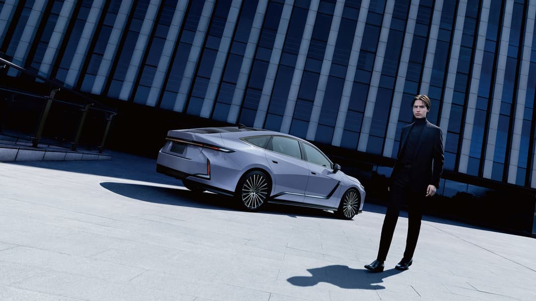 Nouvelle Lexus ES grise garée devant une façade moderne en verre bleu, un homme en costume noir à proximité