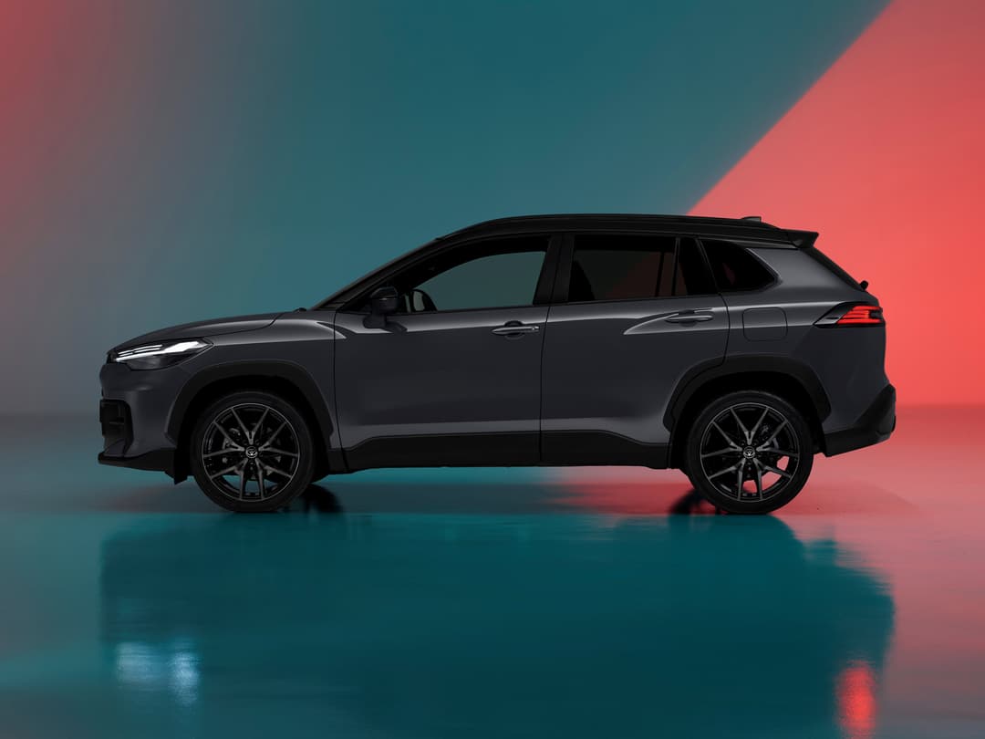 Toyota Corolla Cross gris anthracite de profil avec calandre en nid d'abeilles et feux redessinés sur fond bicolore rose et bleu