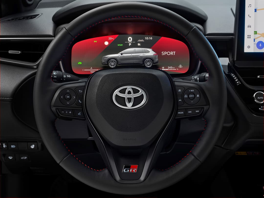 Volant du Toyota Corolla Cross avec écran numérique affichant le mode Sport, le SUV de profil et les données de conduite en rouge et blanc