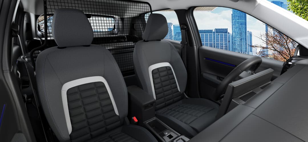 Intérieur de la Citroën Ë-C3 Van avec sièges noirs et blancs, écran tactile et grille de séparation, vue sur des immeubles par les vitres