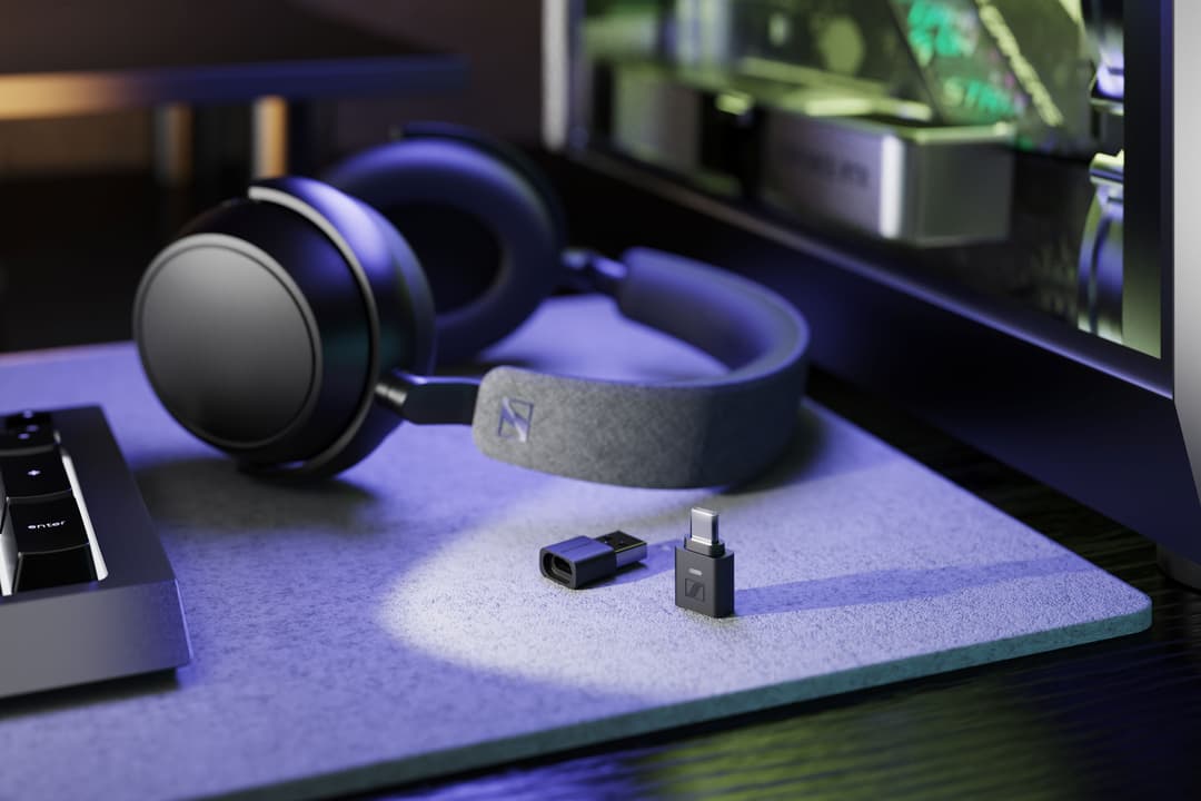 Adaptateur Bluetooth Sennheiser BTD 700 avec ses connecteurs USB et USB-C, entouré d'un casque audio et d'équipements informatiques