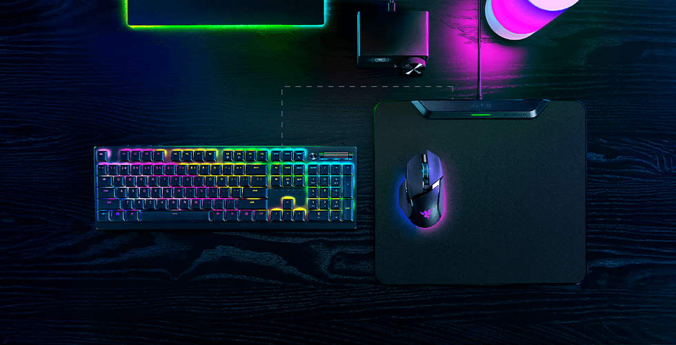 Tapis de souris Razer Hyperflux V2 noir avec souris sans fil gaming posée dessus, aux côtés d'un clavier mécanique RGB illuminé en multicolore