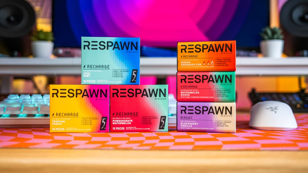 Plusieurs boîtes de RESPAWN by Razer aux couleurs vives bleu, jaune, rose et orange, disposées sur un bureau gaming avec un clavier et une souris