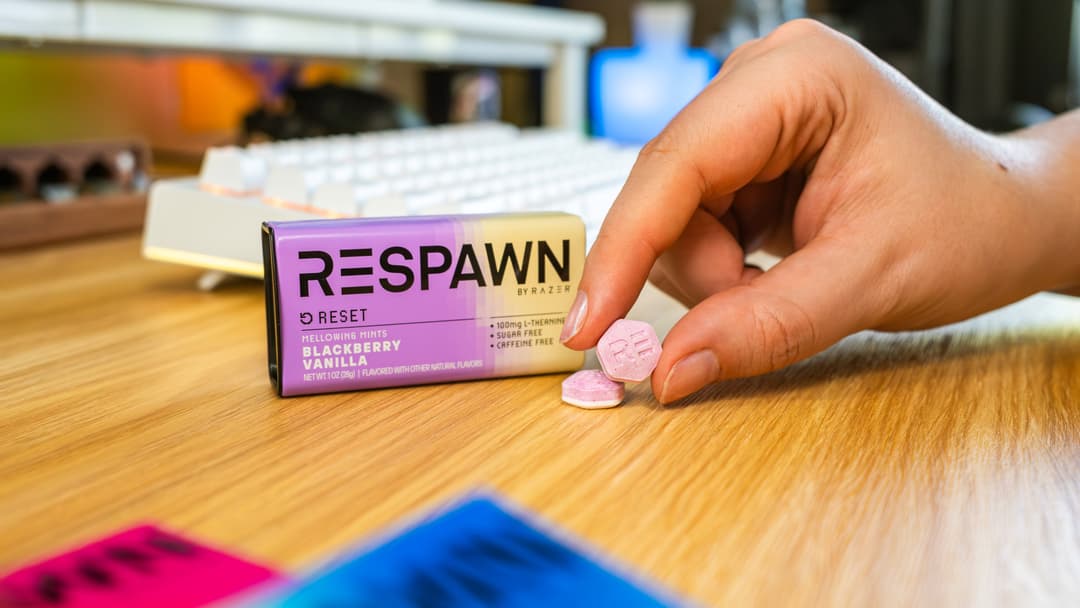 Chewing-gum 5 RESPAWN by Razer saveur blackberry vanilla, boîte rose et jaune, tenu au-dessus d'une surface en bois avec un clavier en arrière-plan