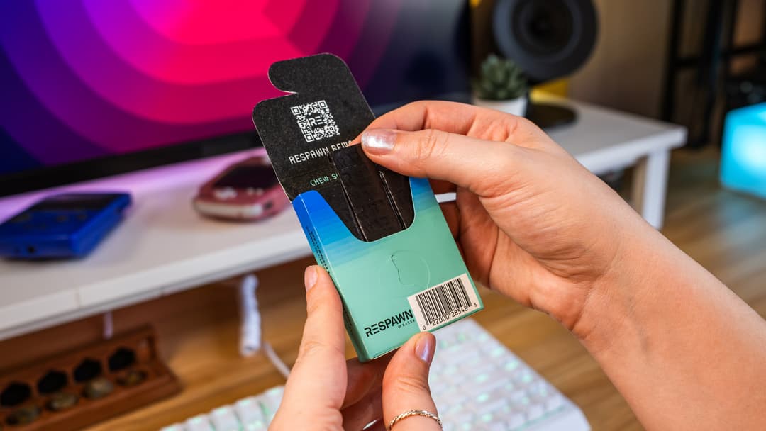 Mains tenant un emballage RESPAWN noir et turquoise avec code QR, dans un environnement de gaming aux néons rose et bleu