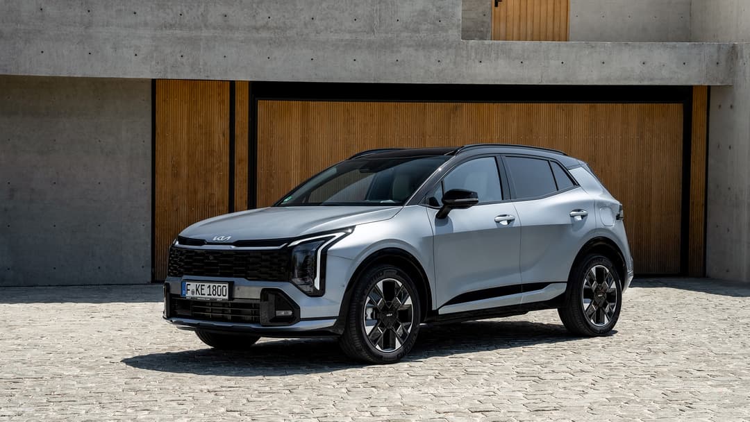 Nouveau Kia Sportage blanc électrique gris clair, SUV compact aux feux LED avant signés Kia, présenté de profil face à un mur de bois