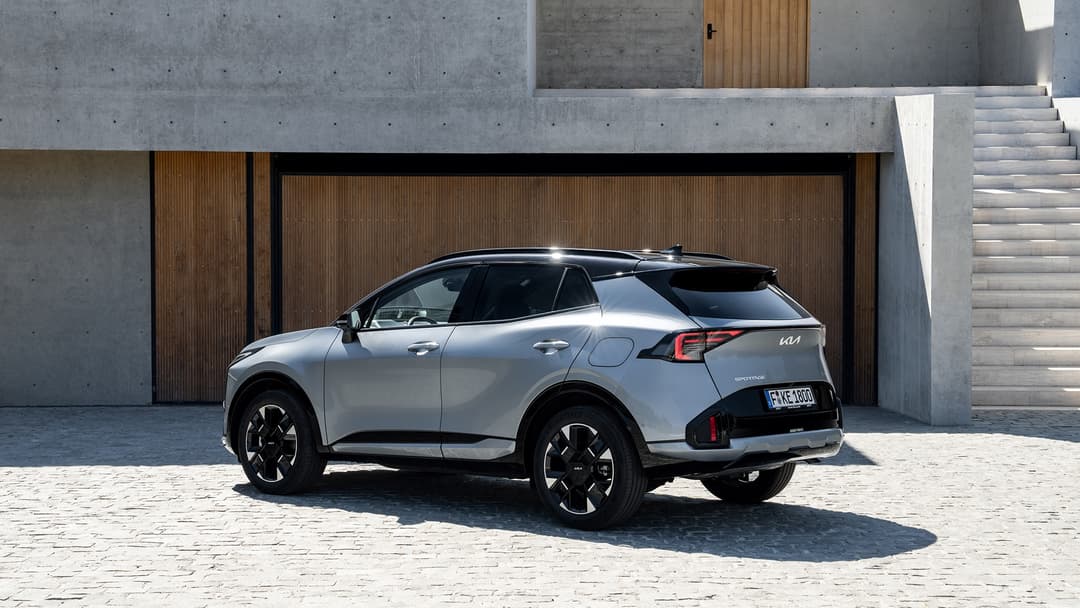 Kia Sportage électrique gris clair, vue de profil, garé devant un bâtiment moderne en béton et bois