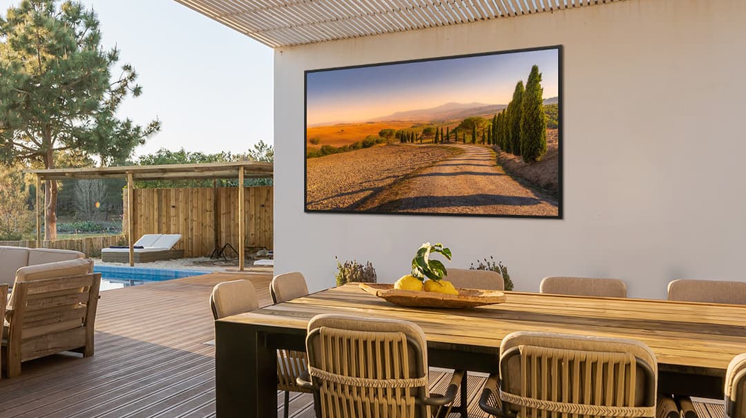 Téléviseur The Terrace accroché à la façade d'une terrasse avec mobilier et piscine, affichant un paysage de Toscane en 4K
