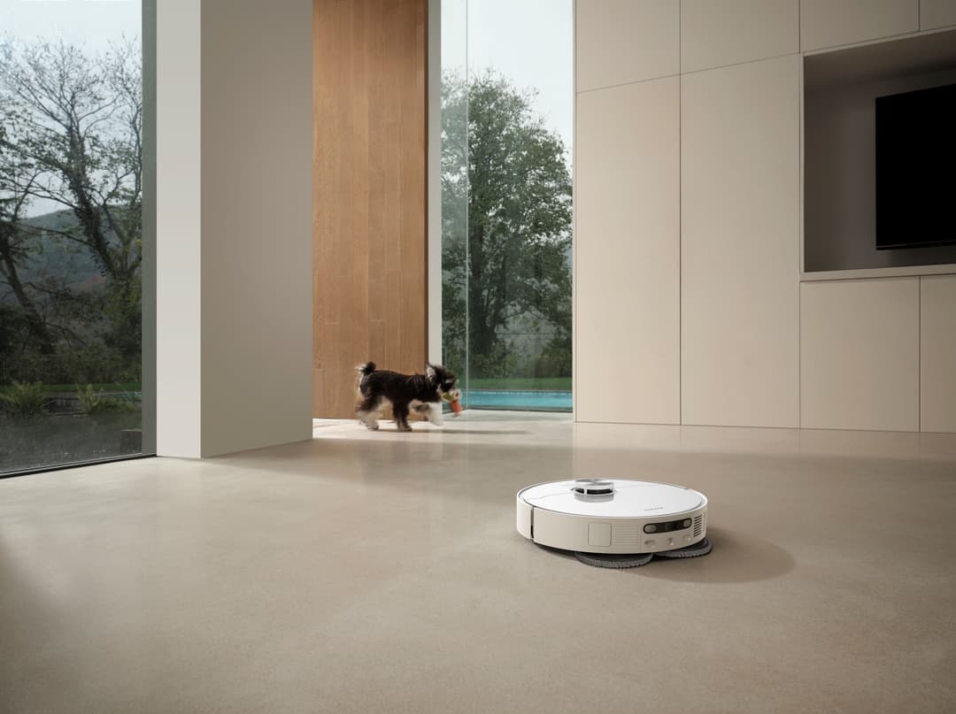 Robot aspirateur laveur Dreame L40 Ultra AE blanc sur sol beige d'une maison moderne, un chien noir en arrière-plan