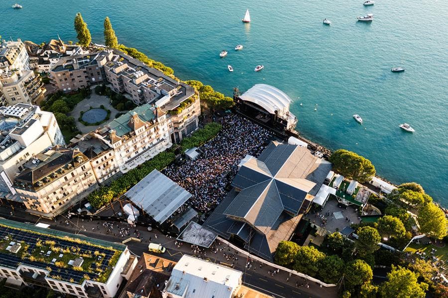 Aérienne de la Scène du Lac du Montreux Jazz Festival avec foule et structures de concert sur le bord du lac Léman turquoise