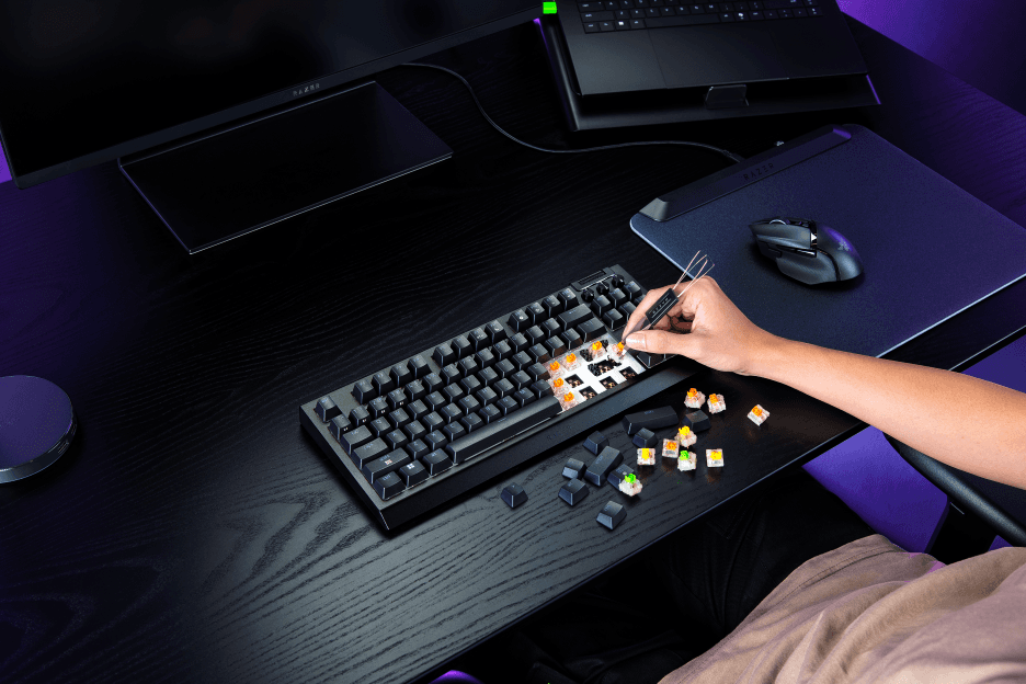 Razer BlackWidow V4 Tenkeyless HyperSpeed avec touches interchangeables colorées disposées à côté, sur un bureau gaming éclairé en violet
