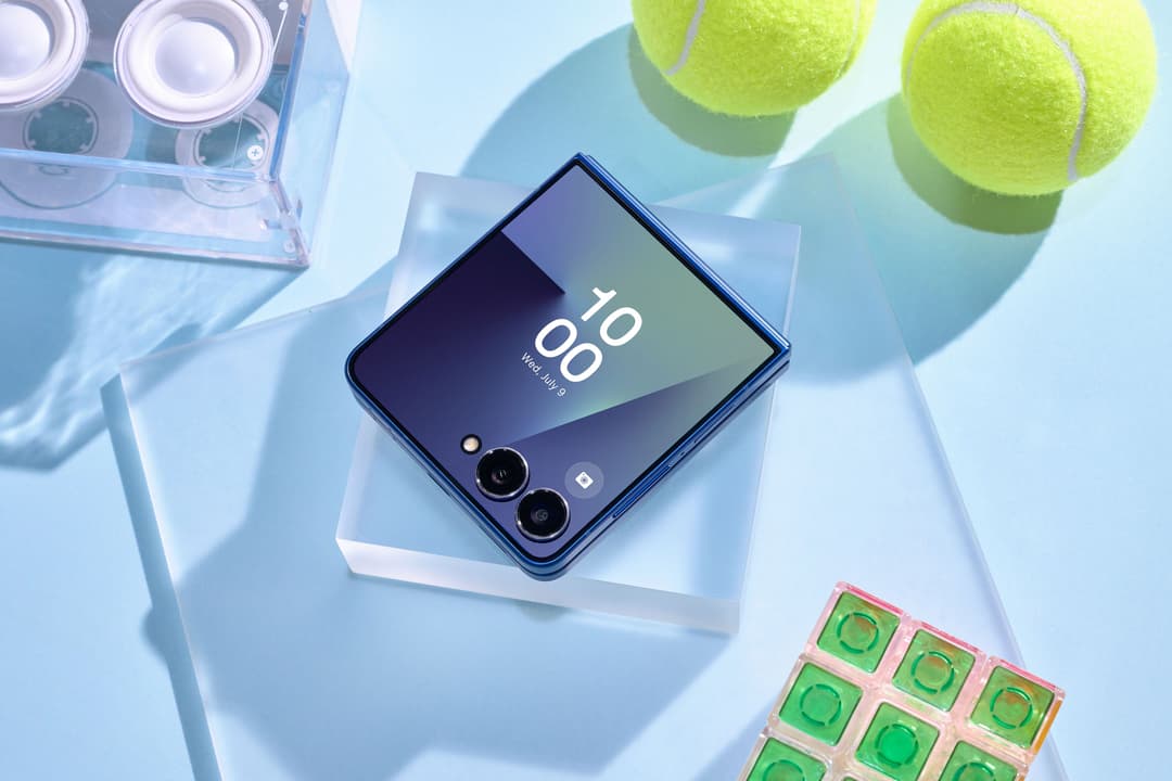Samsung Galaxy Z Flip7 bleu ouvert en position horizontale, affichant l'heure, entouré de balles de tennis jaune-vert et d'accessoires de photographie