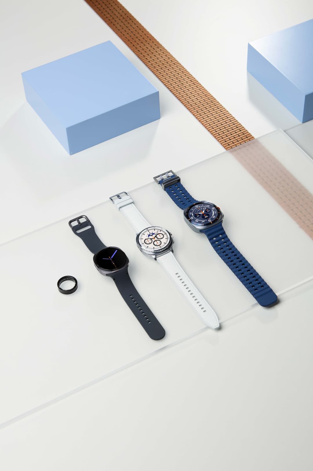 Trois Galaxy Watch8 avec bracelets de couleurs différentes : noir, blanc et bleu, présentées sur fond blanc avec accessoires