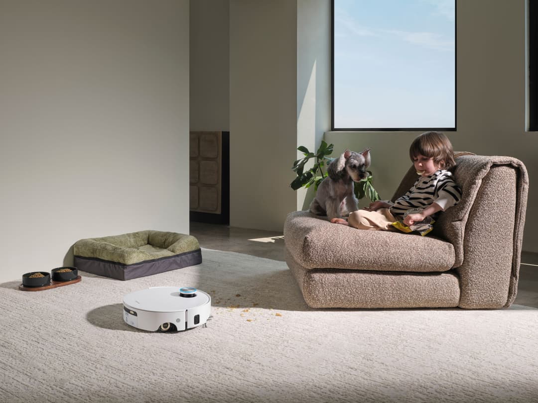 Robot nettoyeur Dreame Aqua10 Ultra Roller Complete blanc sur un tapis clair, dans un salon moderne avec un enfant et un animal assis sur un canapé beige