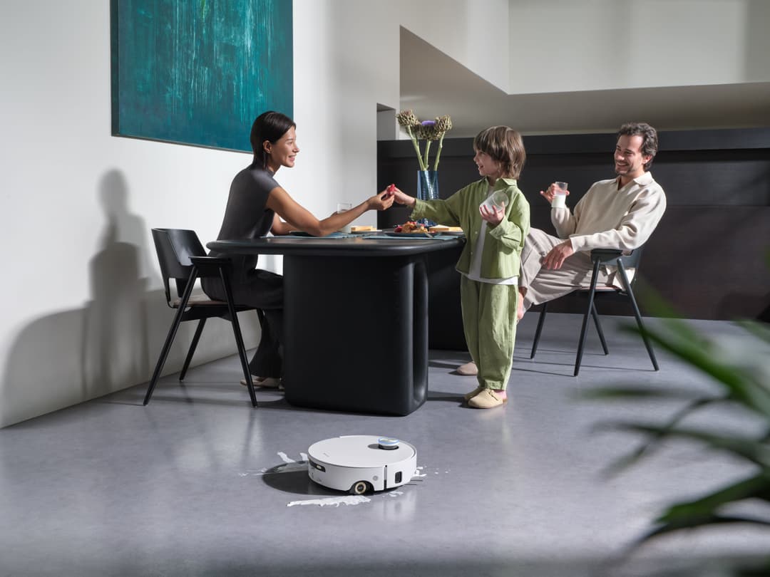 Robot nettoyeur Dreame Aqua10 Ultra Roller Complete blanc sur sol gris, en arrière-plan famille à table dans un intérieur moderne