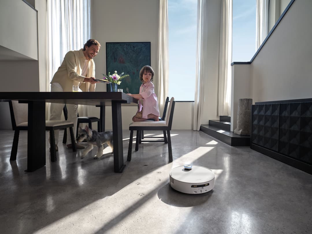 Robot aspirateur Dreame Aqua10 Ultra Roller blanc circulant dans un intérieur minimaliste où un adulte et un enfant se tiennent à une table