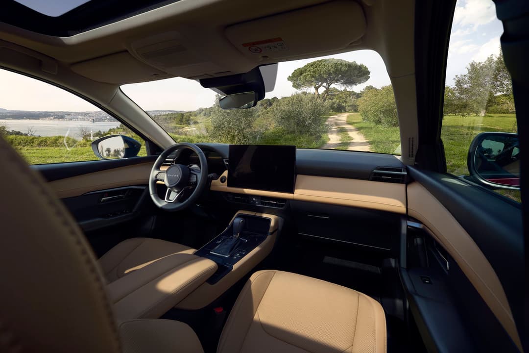 Intérieur du nouveau Mazda CX-5 avec sièges en cuir beige, volant et écran tactile, vue sur paysage rural verdoyant