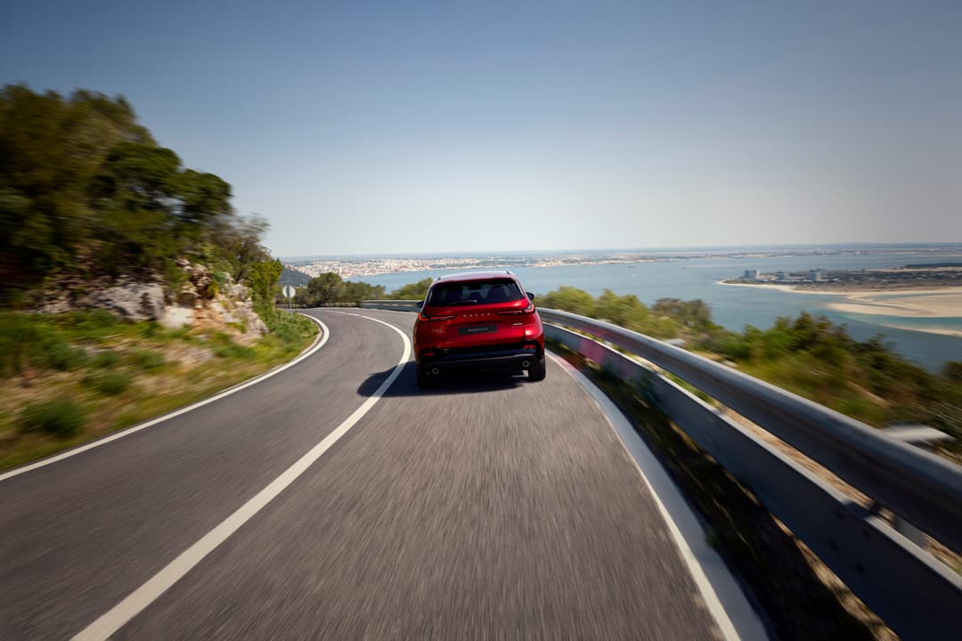 Mazda CX-5 rouge en mouvement sur une route côtière sinueuse avec vue panoramique sur la mer et la côte en arrière-plan