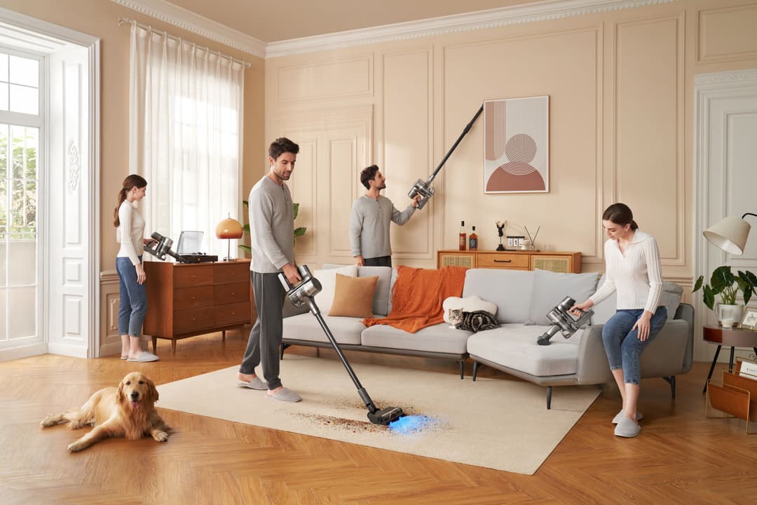 Famille utilisant des aspirateurs sans fil Dreame pour nettoyer un salon beige avec canapé gris, pendant qu'un chien observe
