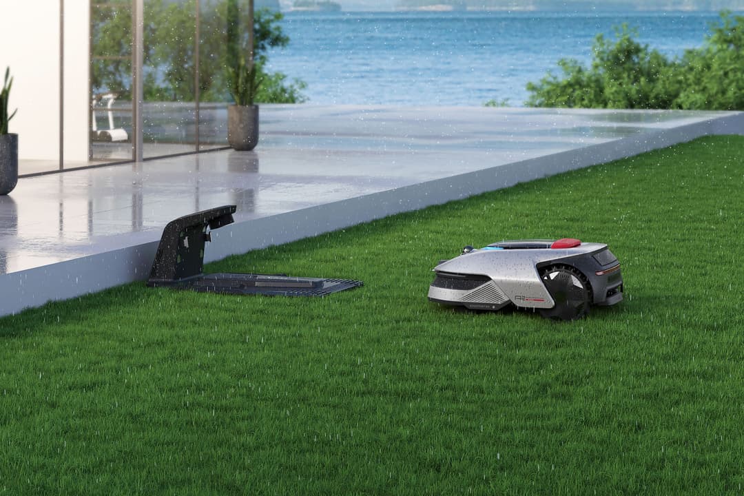 Robot tondeuse automatique Dreame blanc et noir tondant une pelouse verte près d'une piscine et d'une terrasse
