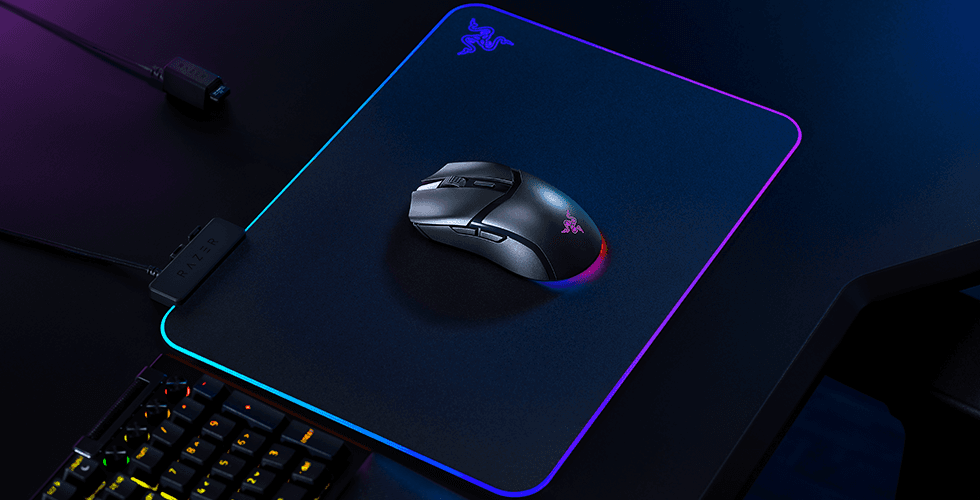 Razer Cobra HyperSpeed, souris sans fil grise et noire avec éclairage RGB sur un tapis Razer, entre clavier et câble USB