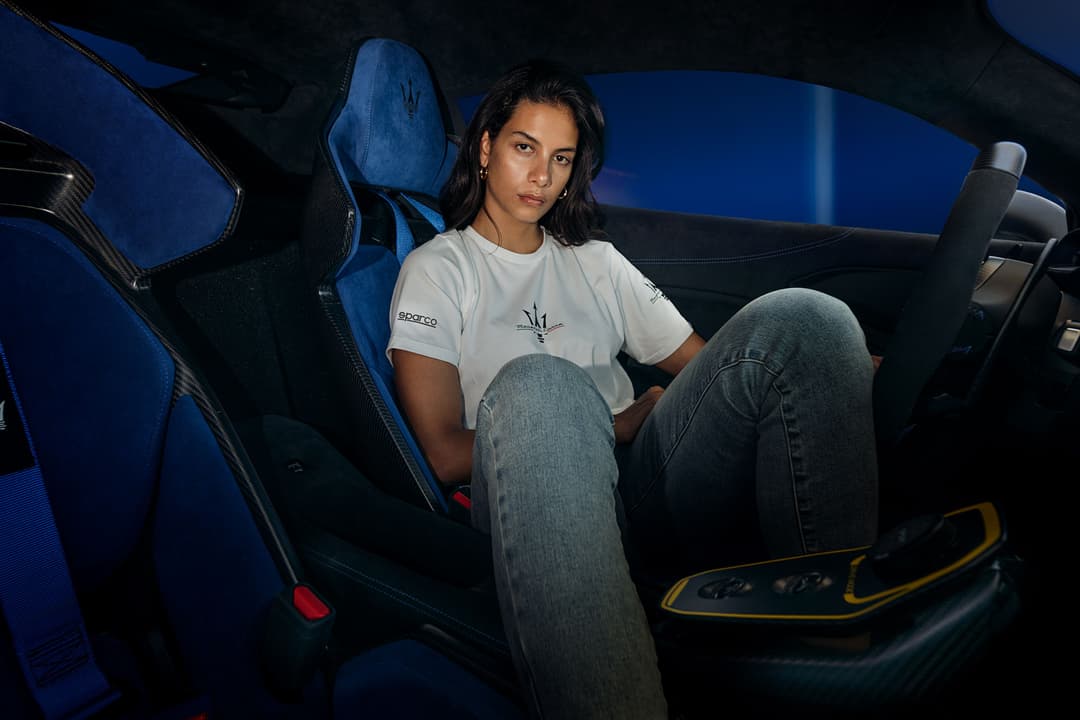 Femme vêtue d'un t-shirt Sparco X Maserati assis dans l'habitacle bleu et noir d'une voiture de sport