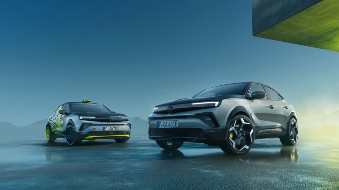 Deux Opel Mokka GSE électriques garés sur un sol mouillé bleu, ciel dégagé en arrière-plan