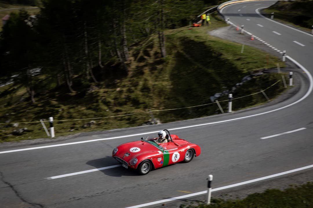 Voiture de course vintage rouge et verte Bernina Gran Turismo circulant sur un col de montagne sinueux entouré de forêts