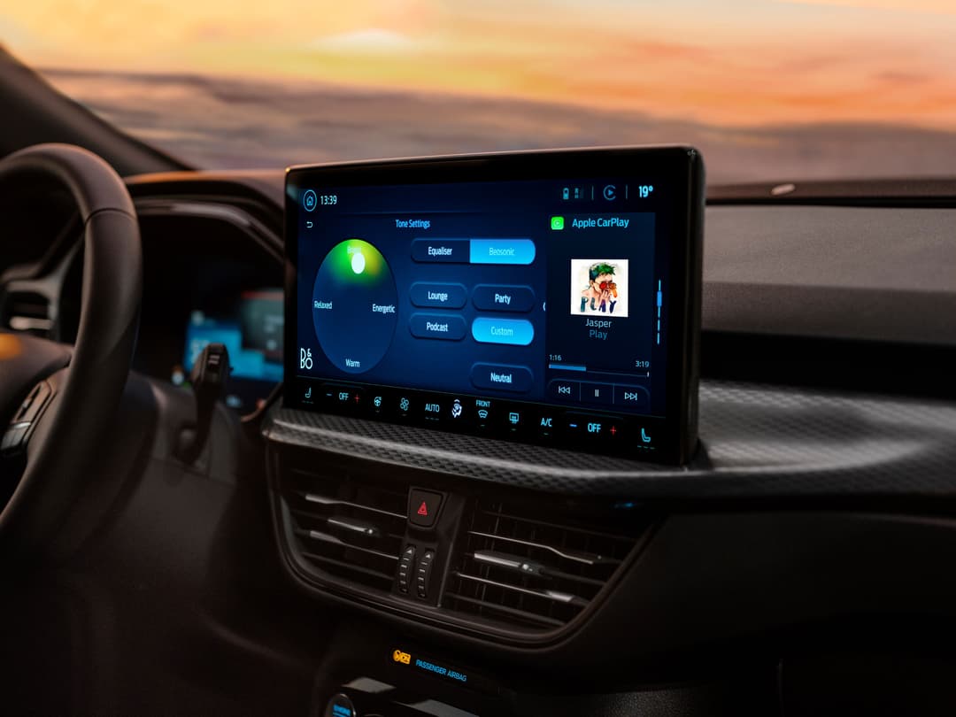 Intérieur du Ford Kuga Sound Edition avec écran tactile affichant les réglages audio et Apple CarPlay, volant noir et tableau de bord contrasté
