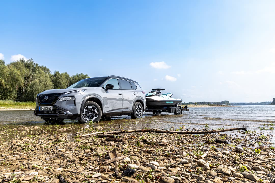 Nissan X-Trail gris tirant un jet-ski au bord d'un lac, sous un ciel bleu dégagé