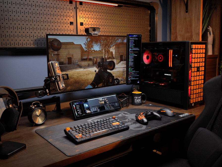 Configuration gaming avec écran CORSAIR XENEON EDGE au centre, flanqué d'un écran secondaire et d'un PC avec ventilateurs rouges, sur un bureau avec clavier et souris CORSAIR