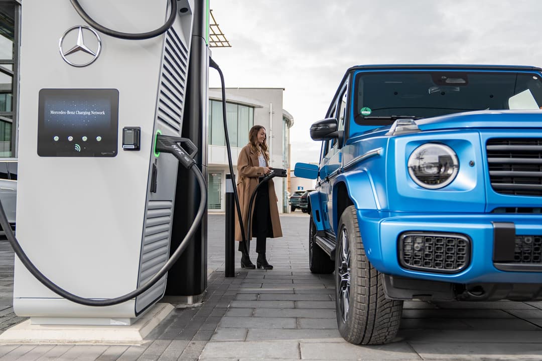 Station de recharge Mercedes pour véhicules électriques avec une femme utilisant l'application mobile et un SUV bleu stationné à proximité