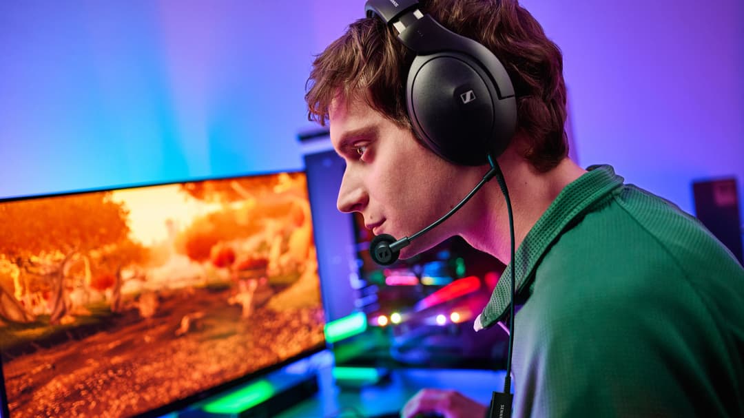Gamer portant un casque Sennheiser noir avec microphone articulé, face à un écran affichant un jeu d'action, ambiance bleue et orange