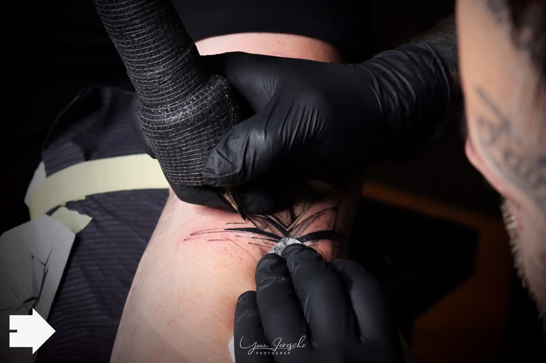 Tatoueur en gants noirs réalisant un tatouage sur l'épaule d'une personne lors de la convention INKvasion