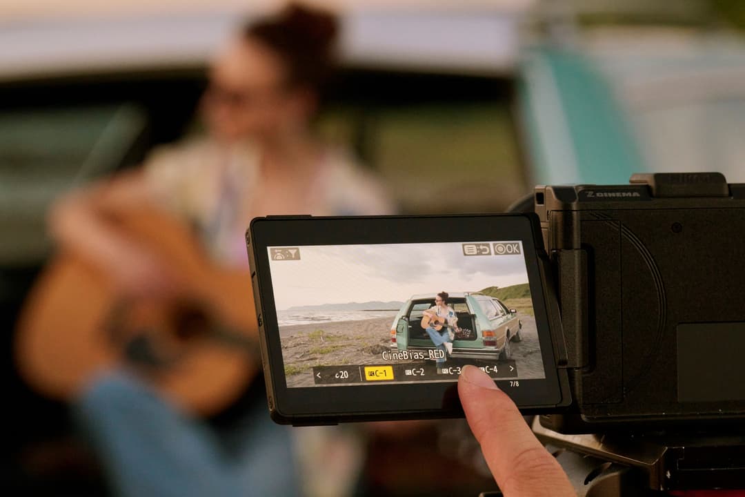 Caméra Nikon RED ZR affichant un plan de tournage côtier sur son écran, opérateur flou en arrière-plan