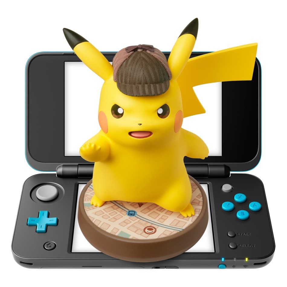 Pikachu jaune portant un chapeau marron de détective, sur une base en bois, devant une Nintendo 3DS ouverte