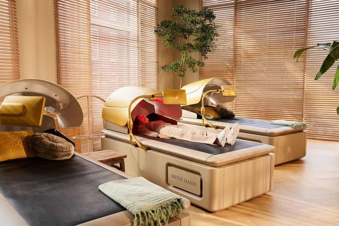 Espace de bien-être Mind Oasis avec lit de massage beige équipé d'accessoires dorés, plantes vertes et volets en bois clair