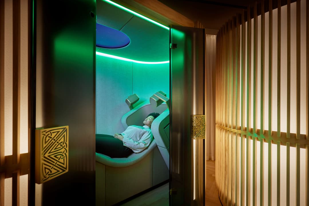 Personne allongée dans un lit de relaxation futuriste aux lumières vertes et bleues du Mind Oasis de Rituals Cosmetics