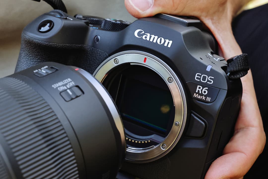 Canon EOS R6 Mark III noir tenu en main avec objectif Canon gris détaché, montrant le capteur et la monture d'objectif