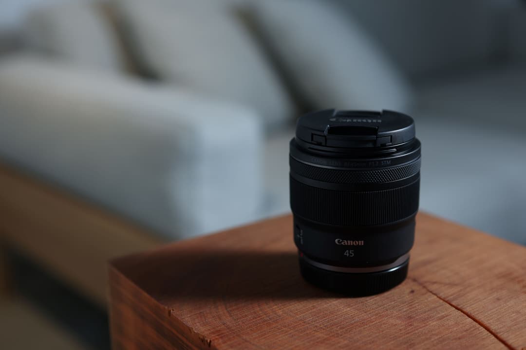 Objectif Canon RF 45 mm F1.2 noir posé sur un plateau en bois, avec un boîtier Canon flou en arrière-plan