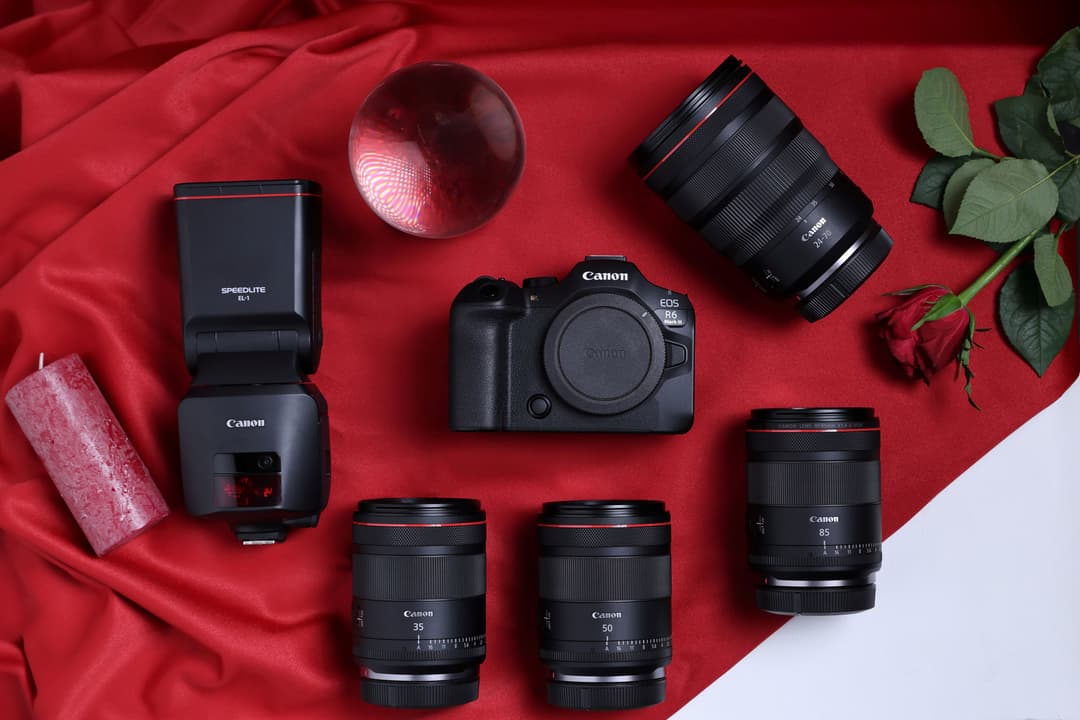 Canon EOS R6 entouré de plusieurs objectifs RF, flash et accessoires, disposés sur fond rouge
