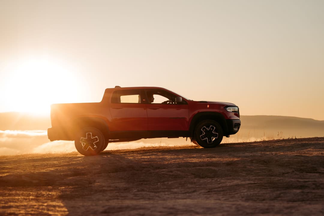 Pick-up RAM Rampage rouge présenté en profil sur un terrain aride au coucher du soleil