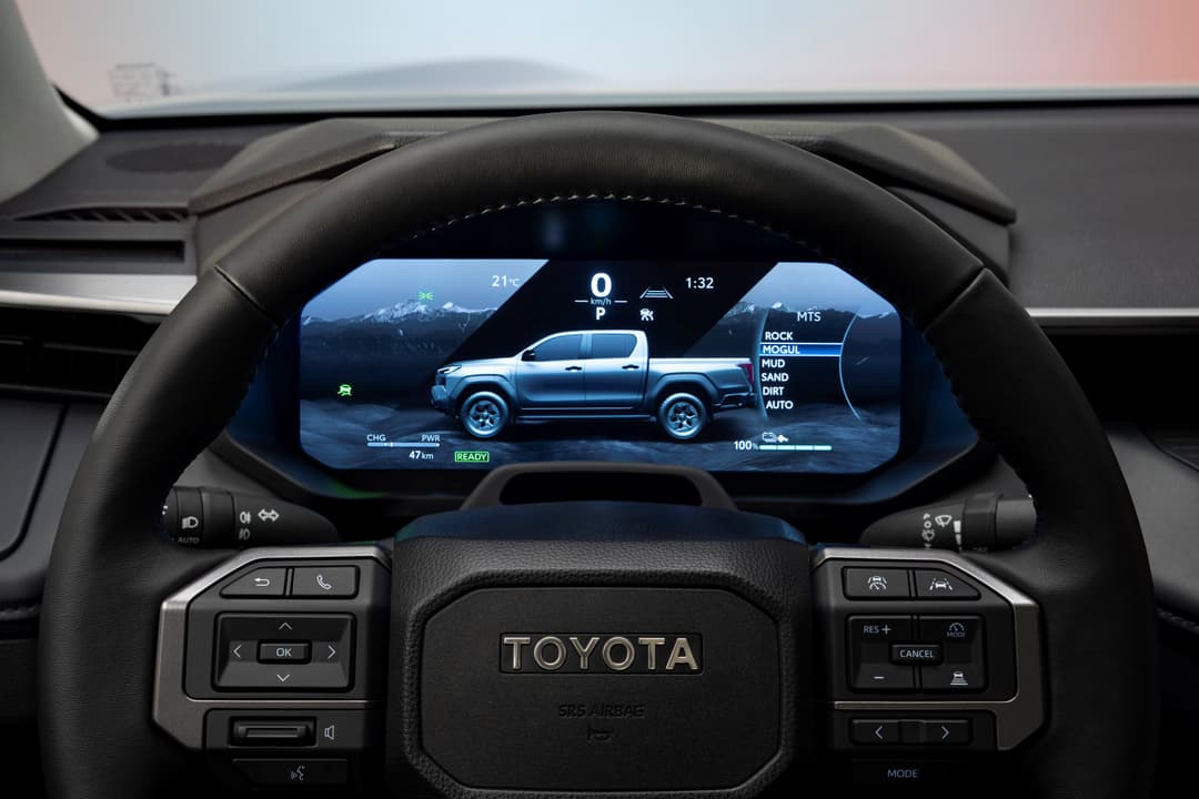 Tableau de bord numérique du Toyota Hilux neuvième génération affichant les données du véhicule électrique avec vue du pick-up bleu dans les montagnes