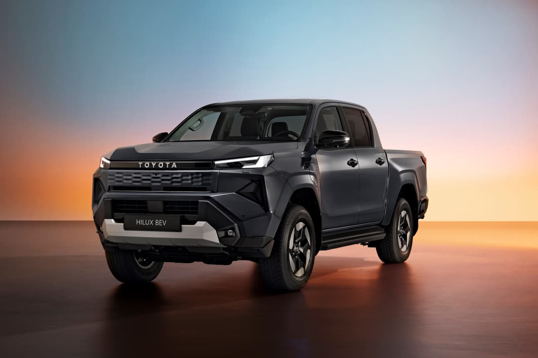 Toyota Hilux BEV, pick-up gris anthracite avec design moderne, photographié de profil sur fond dégradé orange et bleu