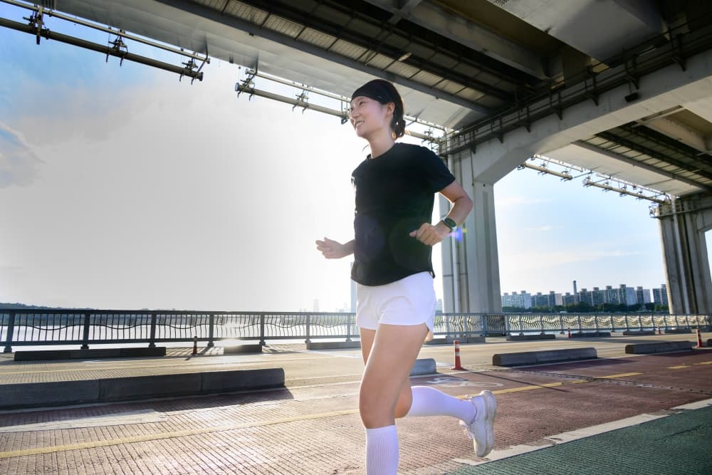 Femme en tenue de sport courant sous un pont, portant une montre connectée Samsung au poignet