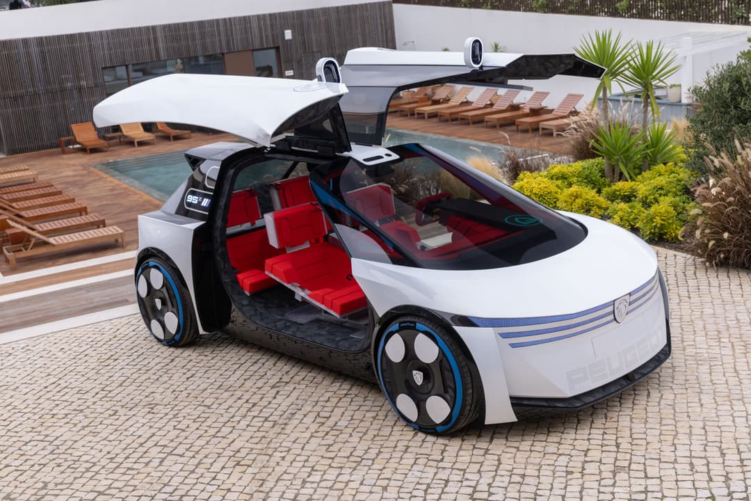Peugeot Polygon Concept, véhicule électrique blanc et bleu avec portes ouvertes, intérieur rouge, roues bleu électrique, stationné devant une maison moderne