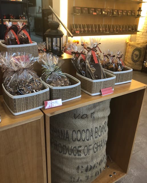 Comptoir de chocolaterie aux tons bois et rouge, présentant des chocolats emballés dans des paniers en jute et des pots en verre